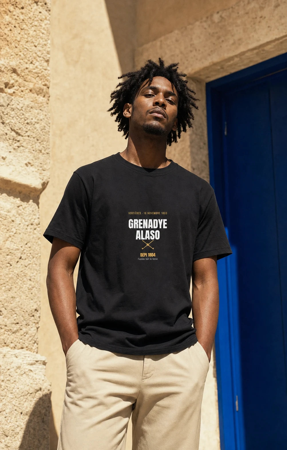 Model wearing the black Grenadye Alaso Vertieres 1803 tee beside a cobalt door